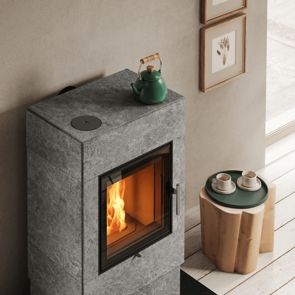 Vue de dessus chaleureuse d'un poêle de masse gris surmonté d'une théière verte, à côté d'une table d'appoint en bois avec des tasses à café.